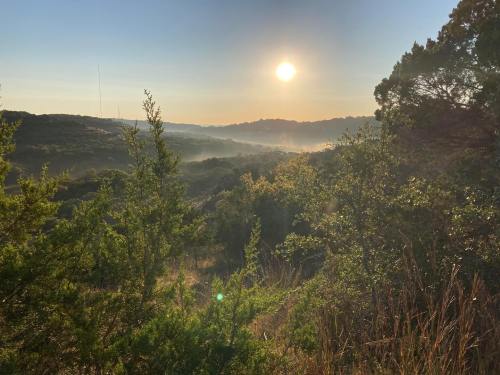 A serene landscape at sunrise, with misty hills and lush greenery under a clear sky.