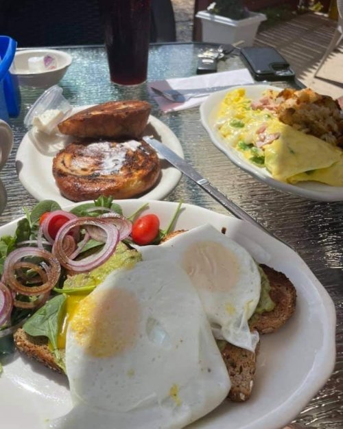 A plate with two fried eggs on toast, salad, cherry tomatoes, and an omelet with sides of cinnamon roll and drink.
