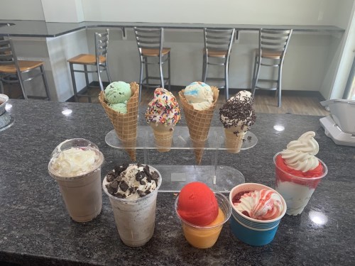 A display of various ice cream cones and cups, featuring colorful scoops, sprinkles, and whipped cream on a countertop.