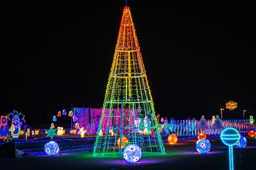Colorful holiday light display featuring a large illuminated tree and various glowing ornaments against a dark night sky.