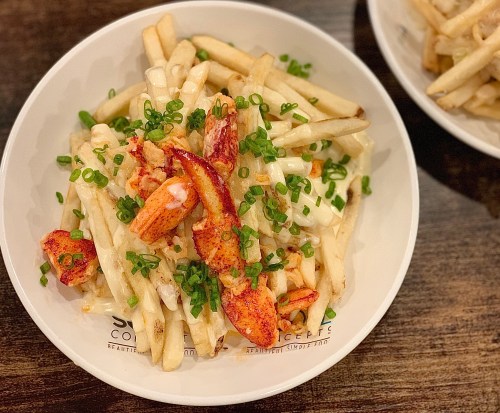 A bowl of fries topped with lobster pieces and chopped green onions.