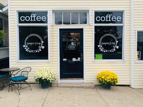 A cozy coffee shop with "coffee" signs in the windows, featuring yellow and white mums outside and an open door.