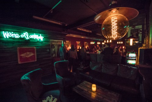 A dimly lit bar with a neon sign, cozy seating, and people socializing in the background.