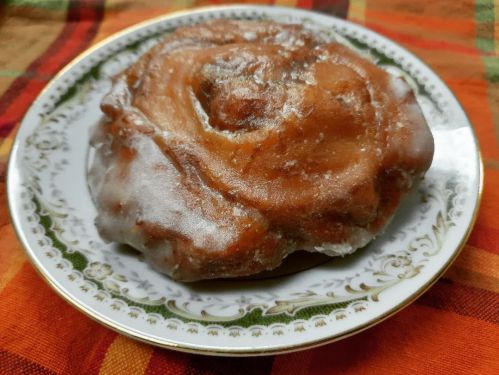A glazed cinnamon roll on a decorative plate, resting on a colorful plaid tablecloth.