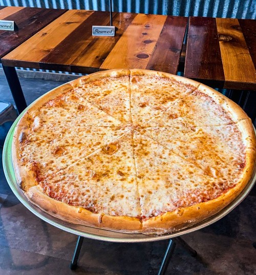 A large cheese pizza on a metal tray, sliced into equal pieces, resting on a wooden table.