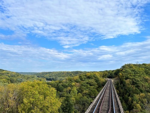 A scenic view of train tracks stretching through lush green trees under a partly cloudy sky.