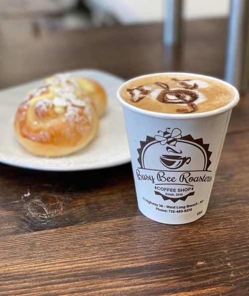 A cup of latte art coffee next to a sweet pastry on a plate, set on a wooden table.
