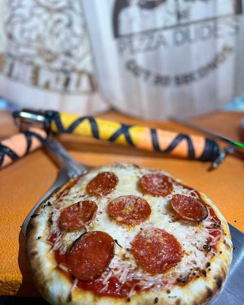 A freshly baked pepperoni pizza on a pizza peel, with colorful decorations in the background.