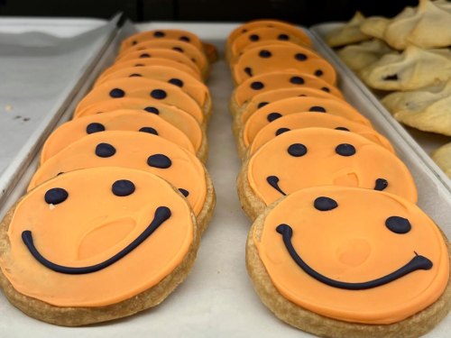 A row of orange smiley face cookies with black icing details on a tray.