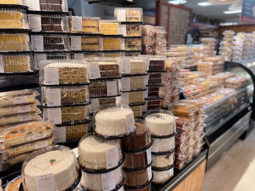 A display of various cakes and desserts stacked in clear containers at a bakery.