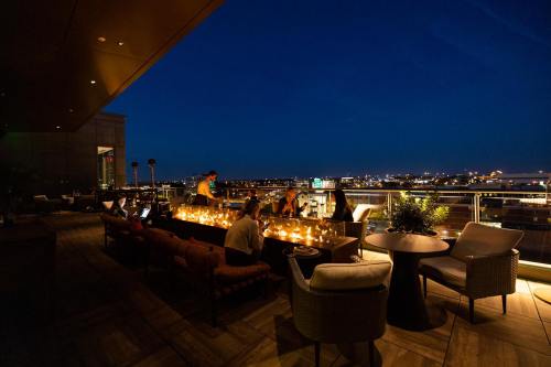 A rooftop bar at night, featuring cozy seating, candles, and city lights in the background.