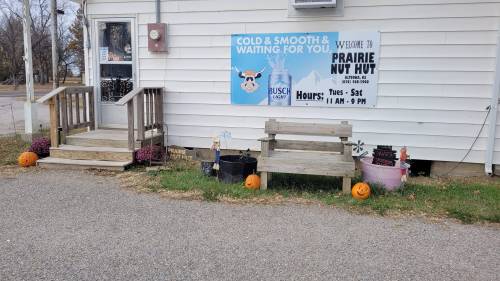 A small storefront with a sign for Prairie Nut Hut, featuring pumpkins and flowers by the entrance.