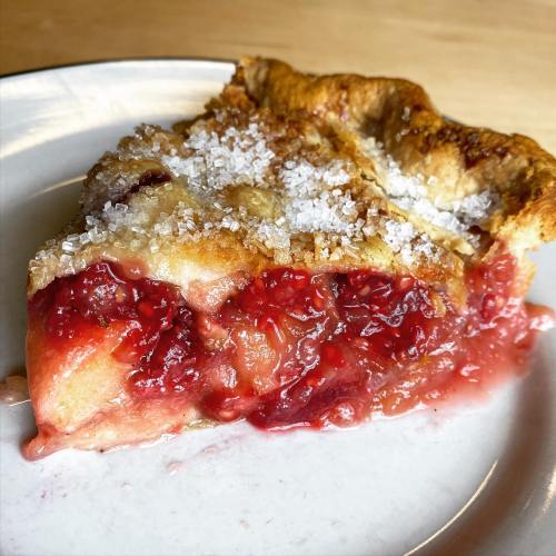A slice of cherry pie with a golden crust, topped with coarse sugar, sitting on a white plate.