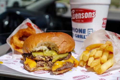 A close-up of a cheeseburger with pickles, fries, onion rings, and a drink on a tray.