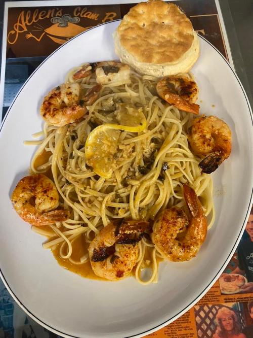 A plate of shrimp pasta with lemon slices and a biscuit, served on a white dish.
