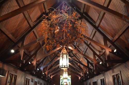 A wooden church interior with a high ceiling, featuring a large, orange floral arrangement hanging above.