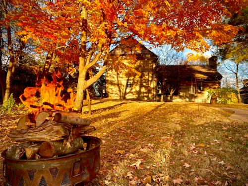 A cozy log cabin surrounded by vibrant autumn foliage and a warm fire pit in the foreground.