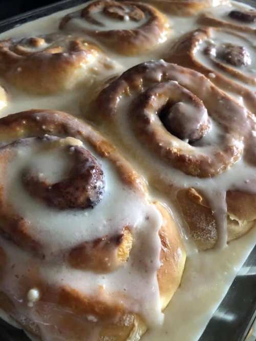 Freshly baked cinnamon rolls drizzled with creamy icing, arranged in a baking dish.