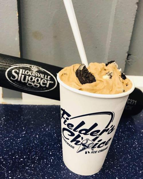 A cup of cookie dough ice cream with an Oreo on top, next to a Louisville Slugger baseball bat.