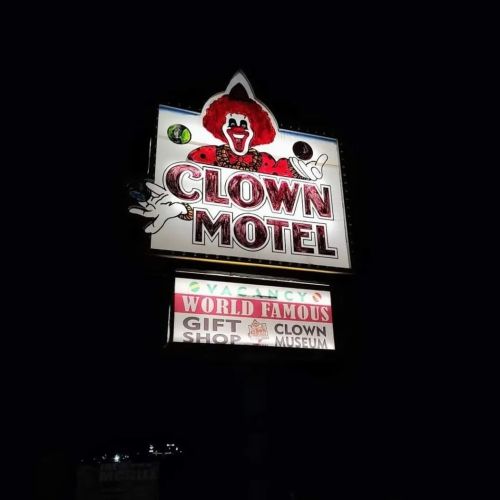 Sign for the Clown Motel featuring a clown graphic, with text about a gift shop and clown museum. Nighttime setting.