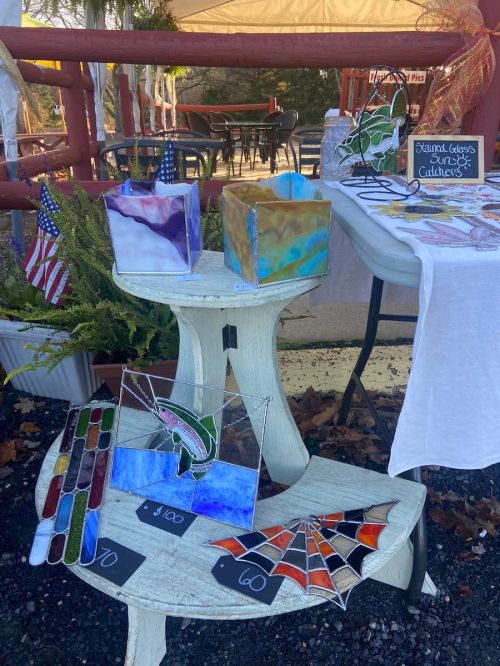 A display of colorful stained glass catchers and decorations on a table, with small American flags in the background.