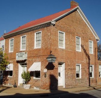 Historic brick building with a red roof, featuring white windows and a sign that reads "Old Brick House."