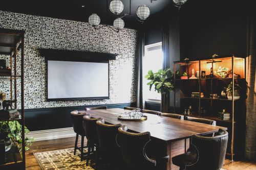 A modern conference room with a large table, stylish chairs, a projector screen, and decorative plants.