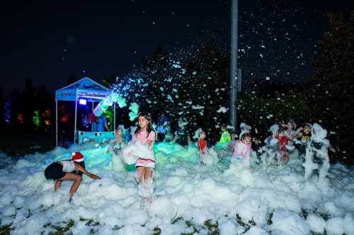 Children playing in a foam party at night, with colorful lights and a festive atmosphere.