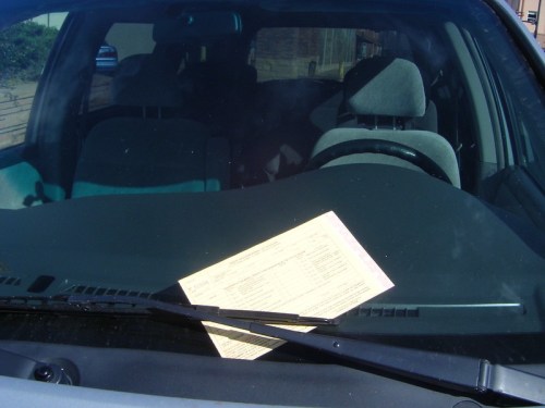 A parking ticket is placed on the windshield of a parked car.