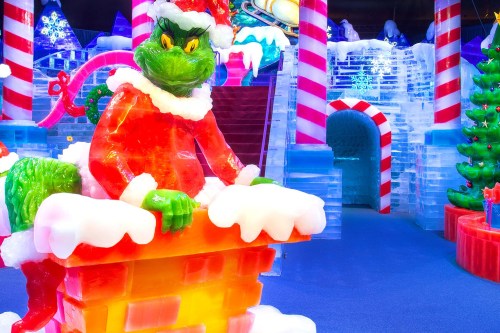 A colorful ice sculpture of the Grinch in a Santa outfit, sitting on a chimney surrounded by festive decorations.