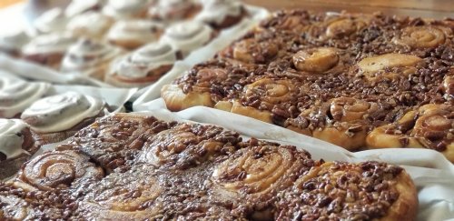 A close-up of two trays of cinnamon rolls, one topped with icing and the other with a pecan caramel glaze.