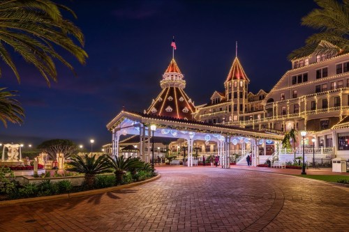 A beautifully lit historic building at night, surrounded by palm trees and festive decorations.