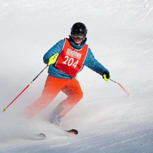 A skier in a bright orange bib and blue jacket navigates a snowy slope, showcasing dynamic movement.