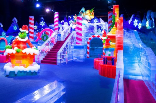Colorful ice sculptures and festive decorations create a whimsical winter wonderland scene with slides and stairs.