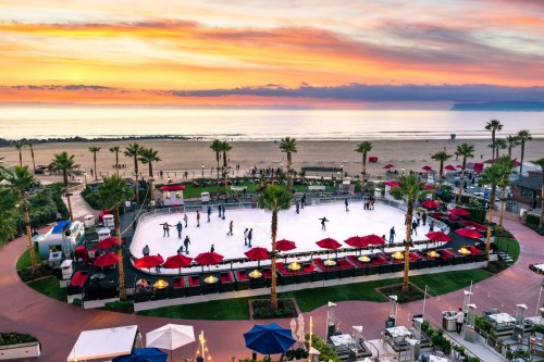 A vibrant sunset over a beachside ice skating rink surrounded by palm trees and red umbrellas.