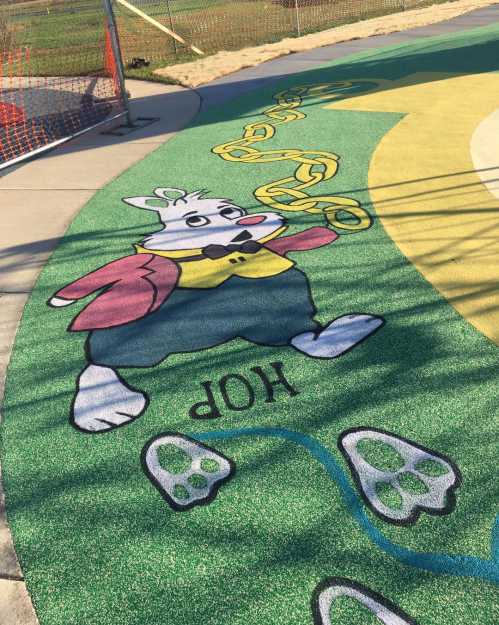 A colorful playground surface featuring a cartoon rabbit in a suit, walking along a path with paw prints and a chain.