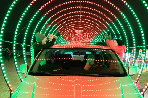 A family enjoys a colorful light display from inside a car, surrounded by vibrant red and green lights.