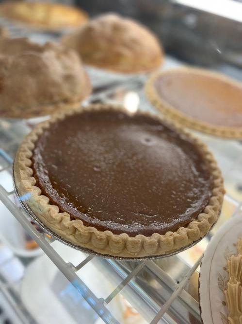 A close-up of a shiny, brown pie with a golden crust, displayed in a glass case among other baked goods.