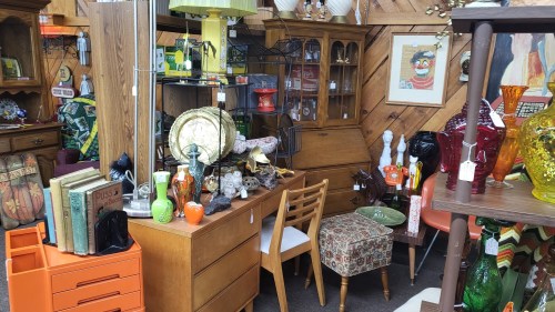 A cozy vintage shop filled with colorful glassware, wooden furniture, and eclectic decor items.
