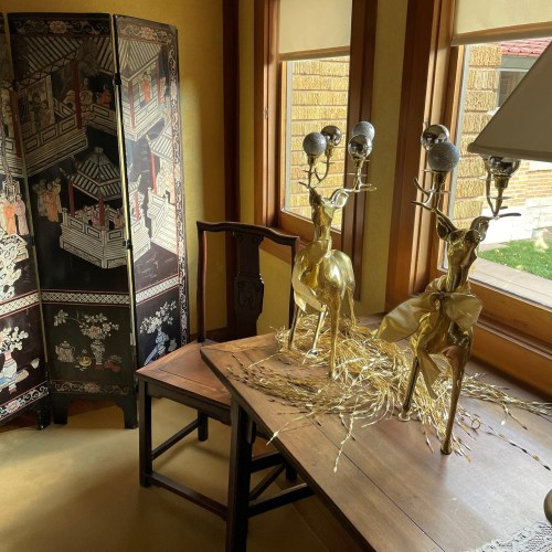 A cozy room featuring a decorative screen, a wooden chair, and two golden deer figurines on a table with straw.