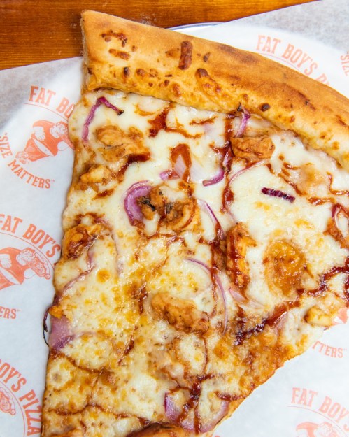 A slice of pizza topped with cheese, red onions, and barbecue sauce on a branded paper plate.
