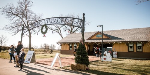 A festive entrance to Echo Village, featuring a sign and visitors enjoying a sunny day outdoors.