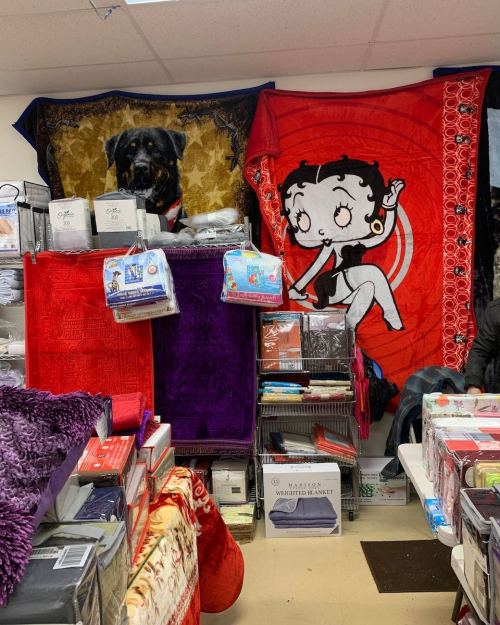 A store display featuring colorful blankets, including a red Betty Boop and a dog-themed blanket, surrounded by various textiles.