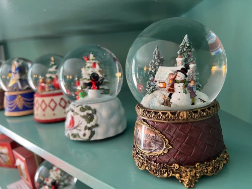 A collection of decorative snow globes featuring winter scenes, displayed on a green shelf.