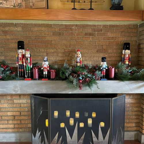 A festive mantel decorated with nutcracker figures, candles, and greenery against a brick wall.