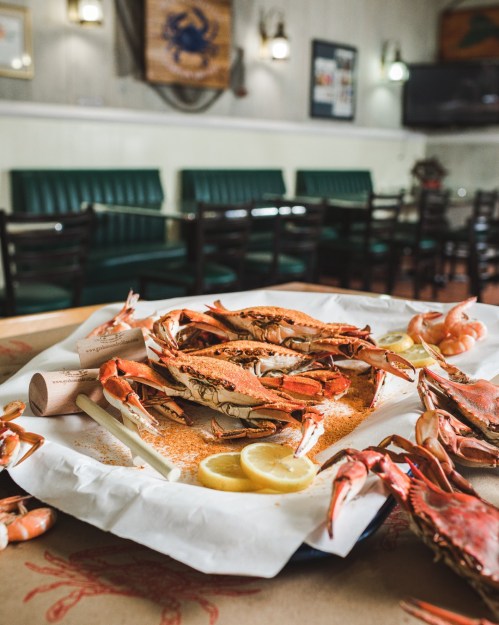 A platter of crabs and shrimp with lemon slices, set on a table in a cozy restaurant with green seating.