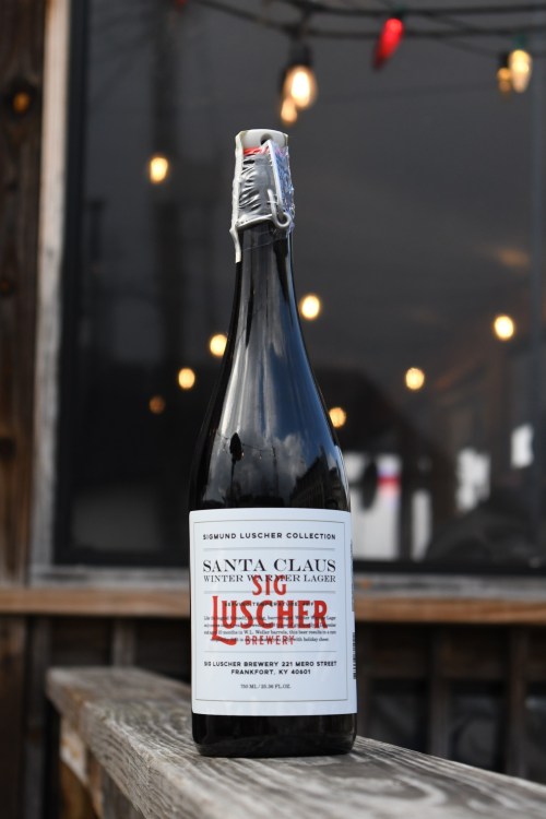 A bottle of Santa Claus Winter Lager from Luscher Brewery, set against a backdrop of string lights.