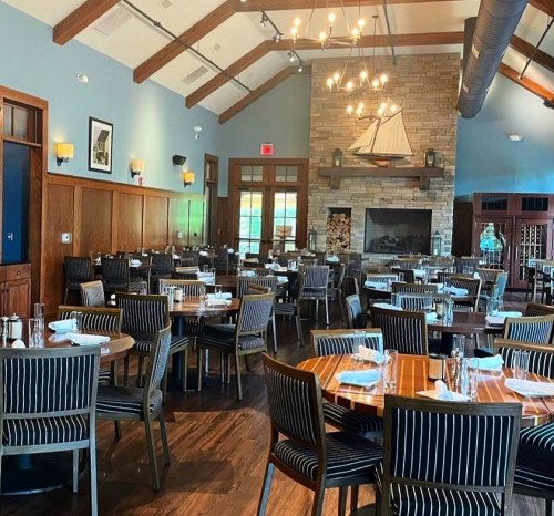 A spacious restaurant interior with wooden tables, striped chairs, and a large fireplace featuring a sailboat decor.