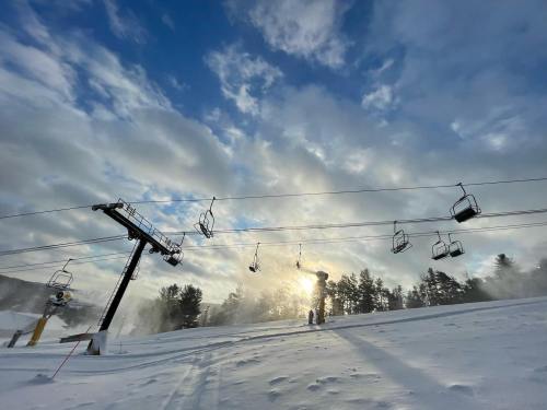Ski lift chairs against a snowy landscape, with sunlight peeking through clouds and trees in the background.