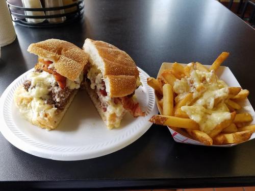 A plate with a sandwich filled with meat, lettuce, and tomato, alongside a serving of cheese fries.